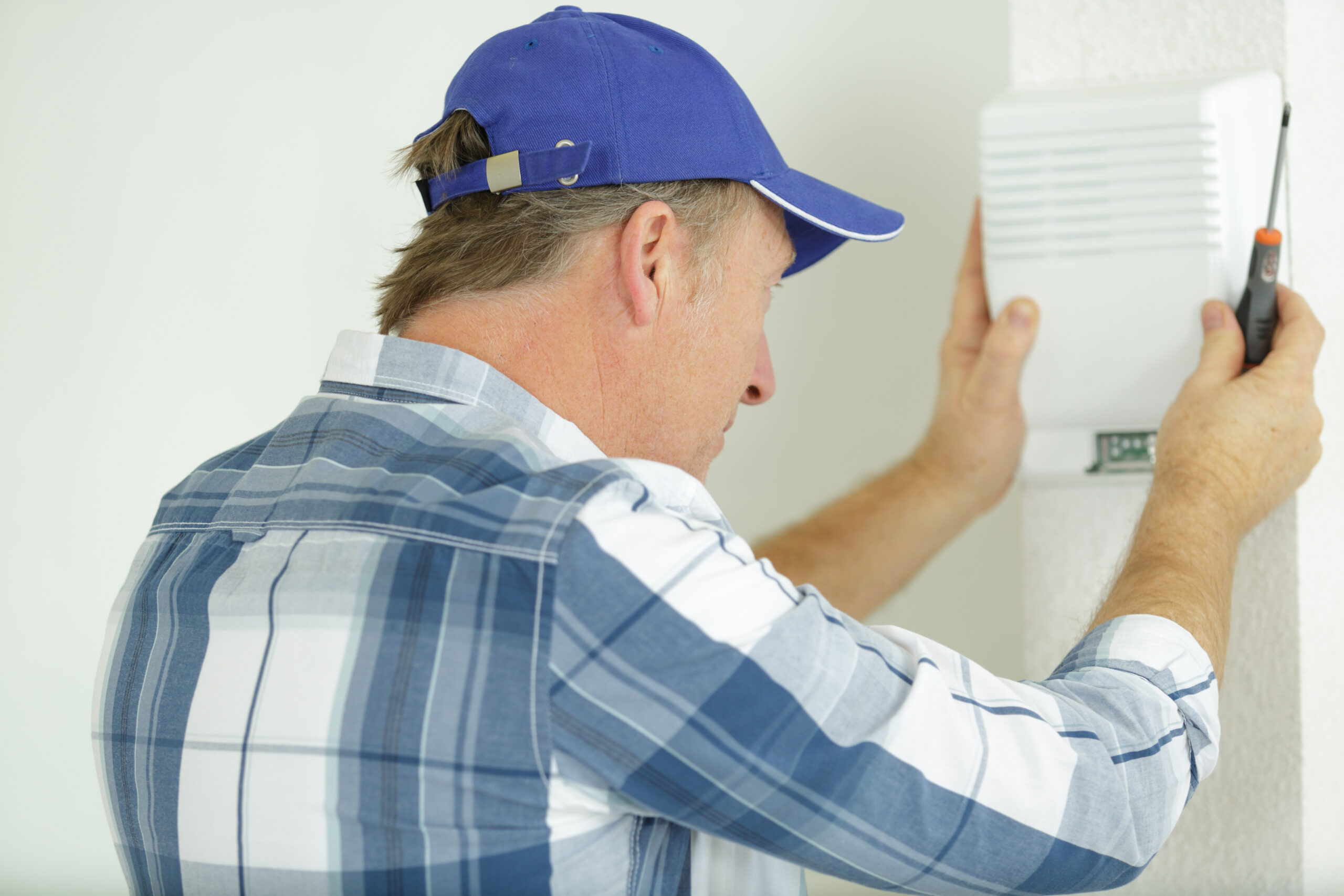 mature tradesman screwing electrical device to wall